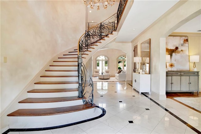 tiled entryway with a chandelier, ornamental molding, and a high ceiling