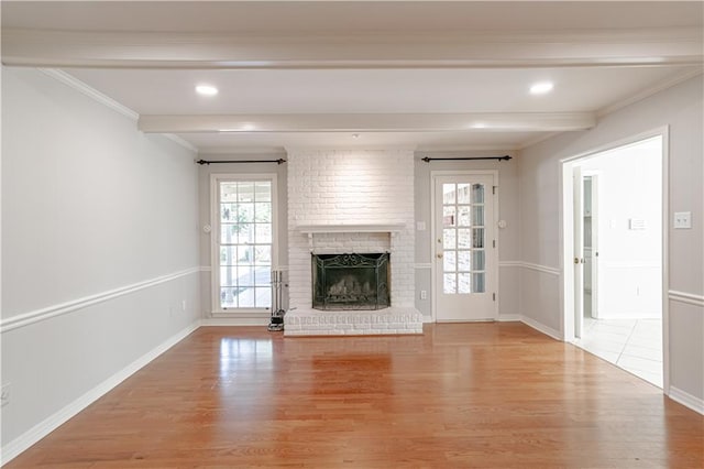 unfurnished living room with beam ceiling, brick wall, a fireplace, and light hardwood / wood-style floors