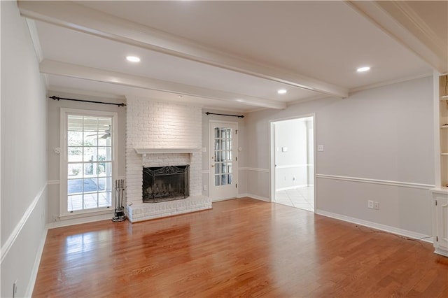 unfurnished living room featuring a fireplace, light hardwood / wood-style flooring, brick wall, and beam ceiling