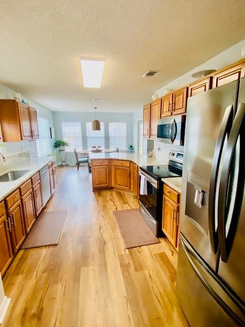 kitchen featuring sink, light hardwood / wood-style flooring, stainless steel appliances, decorative light fixtures, and kitchen peninsula