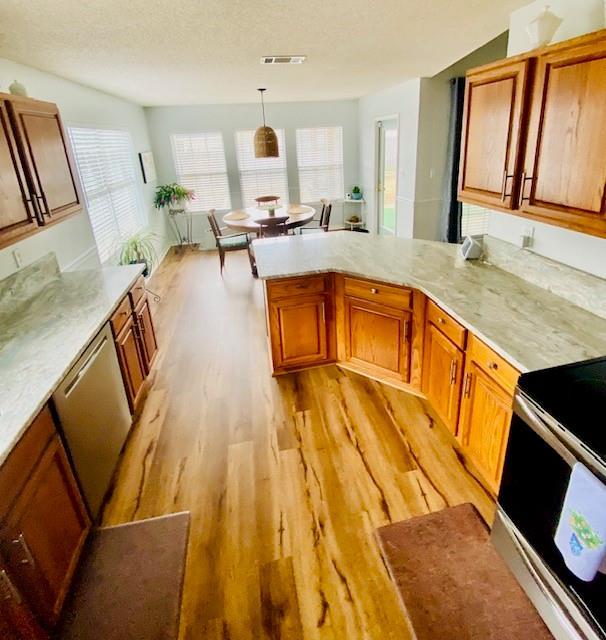 kitchen with decorative light fixtures, light wood-type flooring, kitchen peninsula, stainless steel appliances, and a textured ceiling