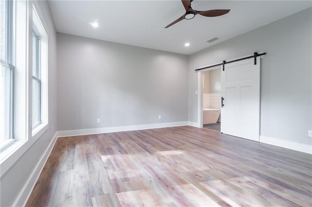 unfurnished bedroom featuring recessed lighting, a barn door, baseboards, visible vents, and wood finished floors