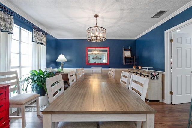 dining room featuring visible vents, a textured ceiling, wood finished floors, crown molding, and a chandelier