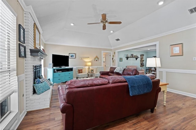 living room with a brick fireplace, wood finished floors, visible vents, and ornamental molding