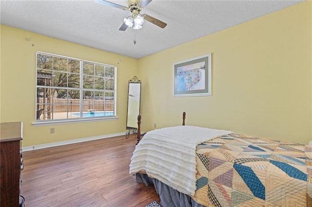 bedroom with a ceiling fan, wood finished floors, baseboards, and a textured ceiling