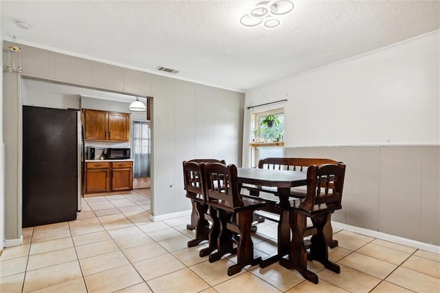 dining area featuring light tile patterned flooring, ornamental molding, and a textured ceiling