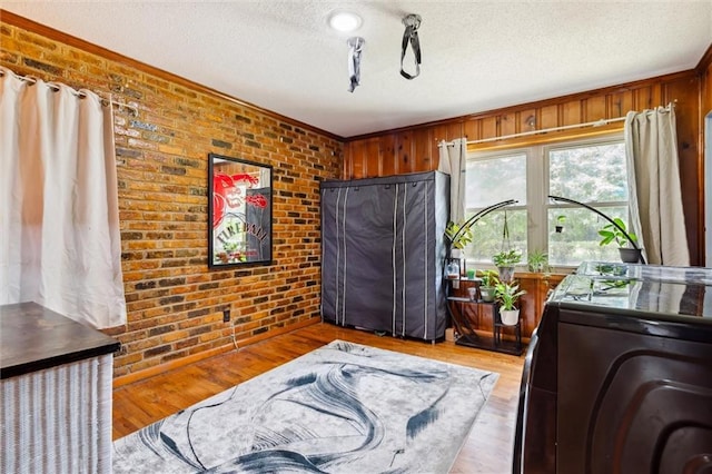 interior space featuring washer / clothes dryer, brick wall, a textured ceiling, and light hardwood / wood-style floors