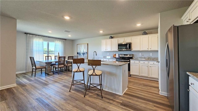 kitchen featuring white cabinets, dark wood-style floors, appliances with stainless steel finishes, and a center island with sink