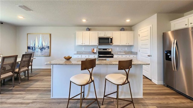 kitchen featuring white cabinets, an island with sink, visible vents, baseboards, and appliances with stainless steel finishes