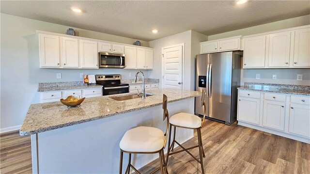 kitchen with light wood-type flooring, white cabinets, a sink, and appliances with stainless steel finishes
