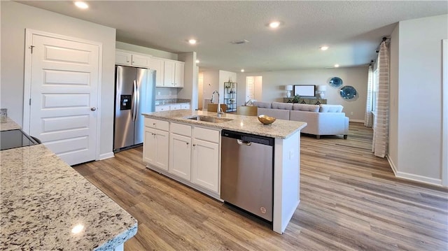 kitchen featuring white cabinets, a sink, open floor plan, light wood-style floors, and appliances with stainless steel finishes