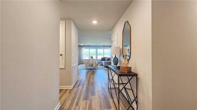 hall featuring wood finished floors, a textured ceiling, baseboards, and a textured wall