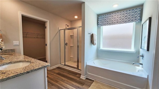full bathroom with a garden tub, wood finished floors, a sink, a stall shower, and a spacious closet