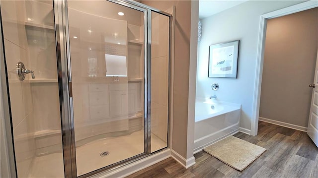 bathroom featuring baseboards, a bath, wood finished floors, and a stall shower