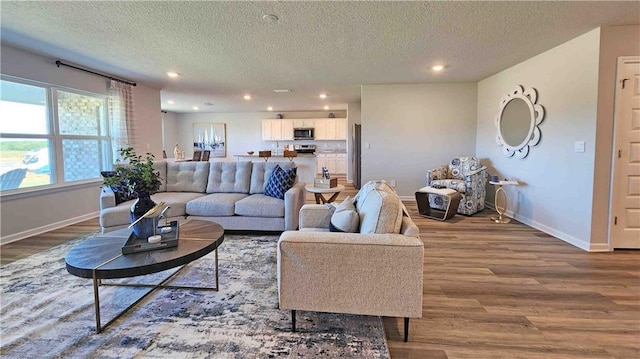 living area with baseboards, wood finished floors, a textured ceiling, and recessed lighting