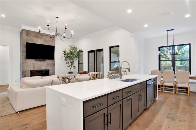 kitchen with a kitchen island with sink, hanging light fixtures, sink, light wood-type flooring, and a chandelier