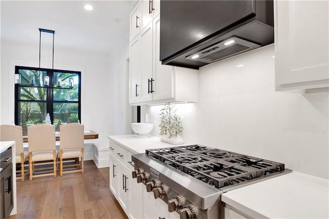 kitchen with light wood-type flooring, custom exhaust hood, stainless steel range, decorative light fixtures, and white cabinets