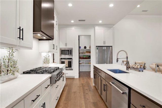 kitchen with white cabinets, sink, wall chimney exhaust hood, light wood-type flooring, and appliances with stainless steel finishes