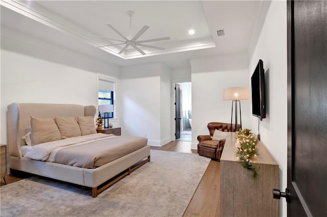 bedroom featuring ceiling fan, wood-type flooring, a tray ceiling, and ensuite bath