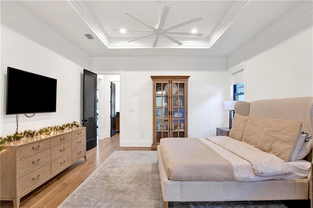 bedroom featuring a raised ceiling, crown molding, and light wood-type flooring