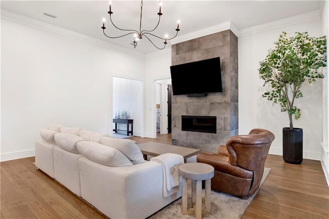 living room featuring a tile fireplace, crown molding, light hardwood / wood-style floors, and a notable chandelier