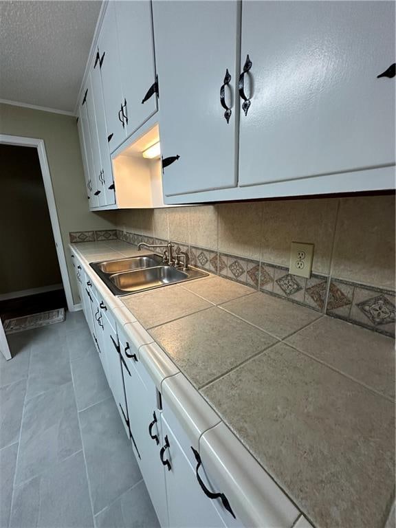 kitchen featuring backsplash, light tile floors, white cabinets, sink, and a textured ceiling