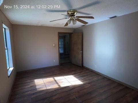 empty room featuring a healthy amount of sunlight, a textured ceiling, ceiling fan, and dark wood-type flooring