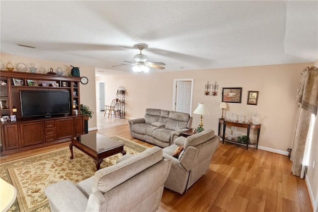 living room featuring ceiling fan, light hardwood / wood-style floors, and a textured ceiling