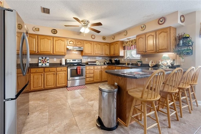 kitchen with a breakfast bar area, kitchen peninsula, ceiling fan, stainless steel appliances, and decorative backsplash