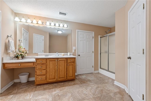 bathroom with vanity, a shower with shower door, and a textured ceiling