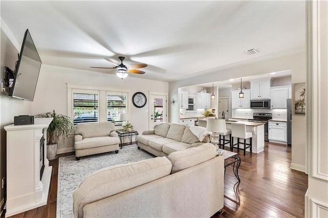 living area with dark wood-style floors, a ceiling fan, visible vents, and baseboards