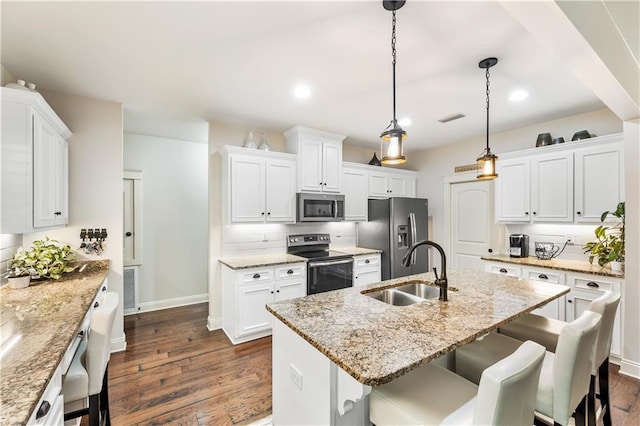 kitchen with dark wood-style floors, a sink, a kitchen breakfast bar, baseboards, and appliances with stainless steel finishes