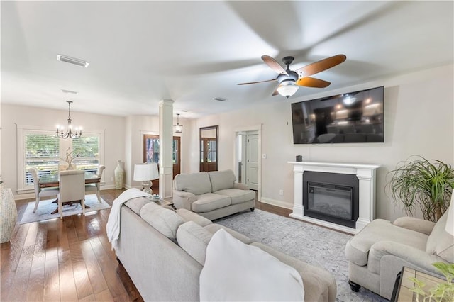 living room with dark wood-type flooring, visible vents, baseboards, and ceiling fan with notable chandelier