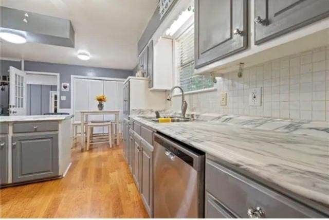 kitchen with gray cabinetry, sink, light hardwood / wood-style flooring, stainless steel dishwasher, and tasteful backsplash