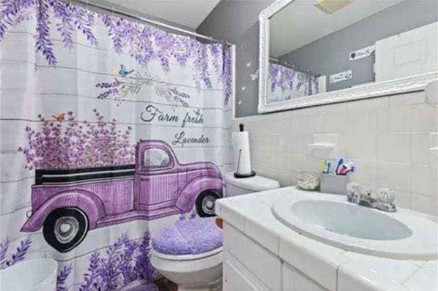 bathroom with backsplash, vanity, tile walls, and toilet