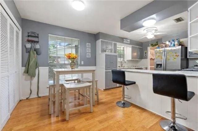 kitchen featuring a breakfast bar, stainless steel fridge, light wood-type flooring, and white cabinetry