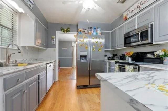 kitchen featuring light stone counters, gray cabinetry, stainless steel appliances, sink, and light hardwood / wood-style floors