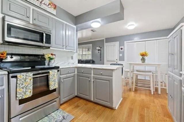 kitchen featuring gray cabinets, kitchen peninsula, stainless steel appliances, and light wood-type flooring