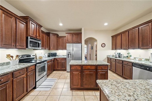 kitchen featuring light stone counters, light tile patterned flooring, stainless steel appliances, and a kitchen island