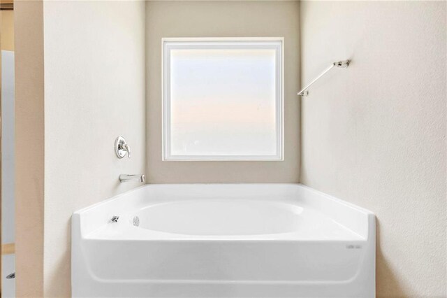 full bath featuring a garden tub, a textured wall, and a healthy amount of sunlight