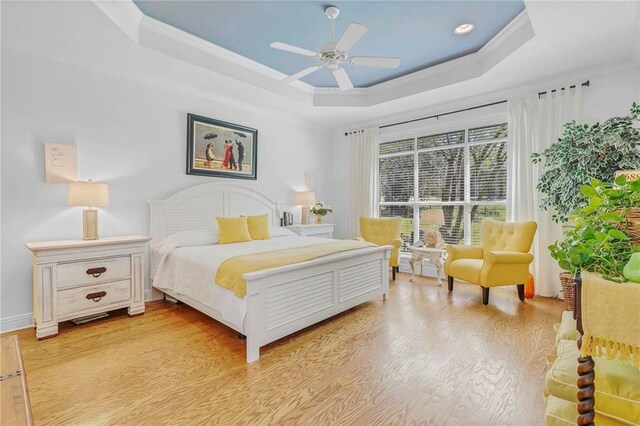bedroom featuring a ceiling fan, baseboards, ornamental molding, a raised ceiling, and light wood-type flooring