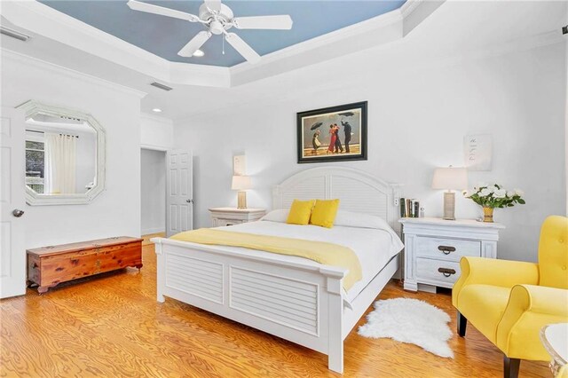bedroom featuring light wood finished floors, visible vents, crown molding, and a raised ceiling