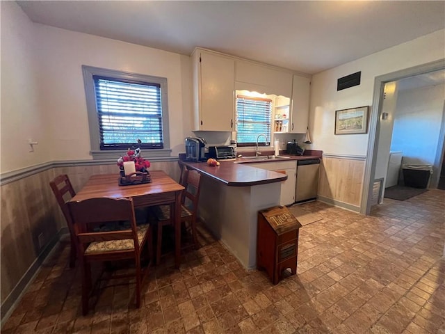 kitchen featuring stainless steel dishwasher, wood walls, white cabinets, and sink