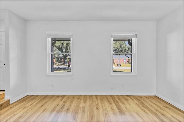 empty room featuring a wealth of natural light, baseboards, and wood finished floors