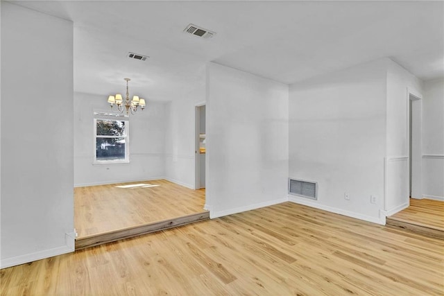 spare room with baseboards, wood finished floors, visible vents, and a notable chandelier