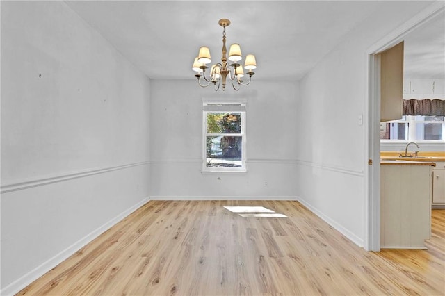 unfurnished dining area featuring a chandelier, a sink, light wood-style flooring, and baseboards