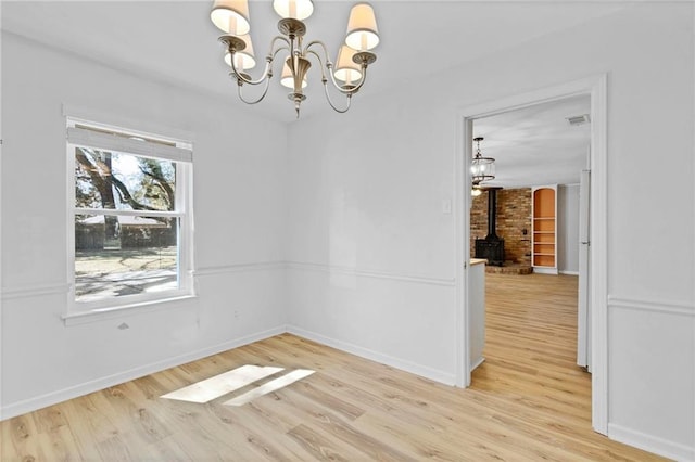 unfurnished dining area featuring light wood finished floors, visible vents, baseboards, a wood stove, and a notable chandelier