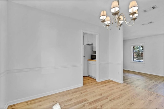 unfurnished dining area featuring light wood finished floors, baseboards, visible vents, and a notable chandelier