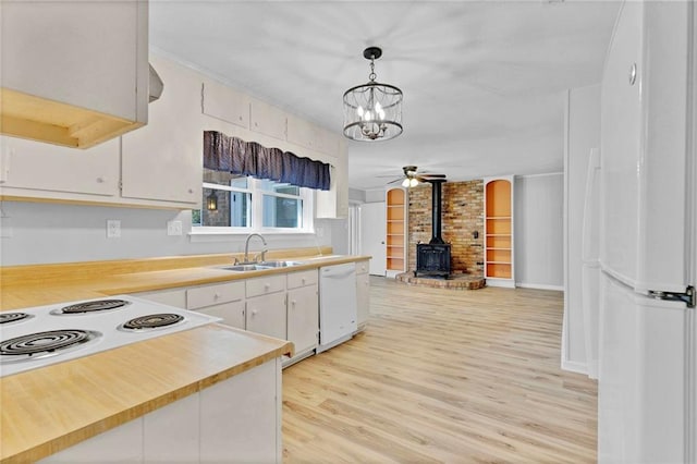 kitchen with white appliances, light wood finished floors, a wood stove, light countertops, and a sink