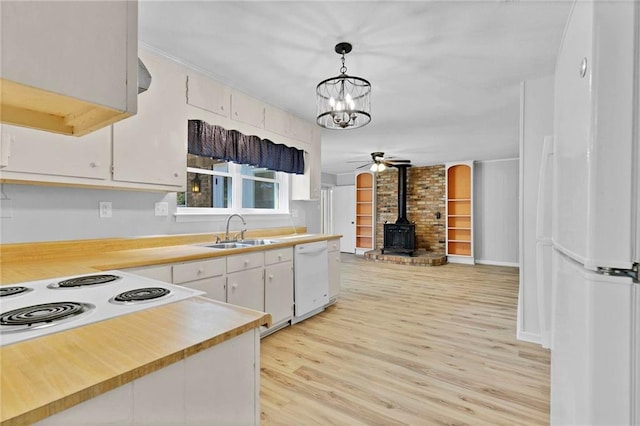 kitchen featuring white appliances, a sink, light countertops, light wood finished floors, and a wood stove